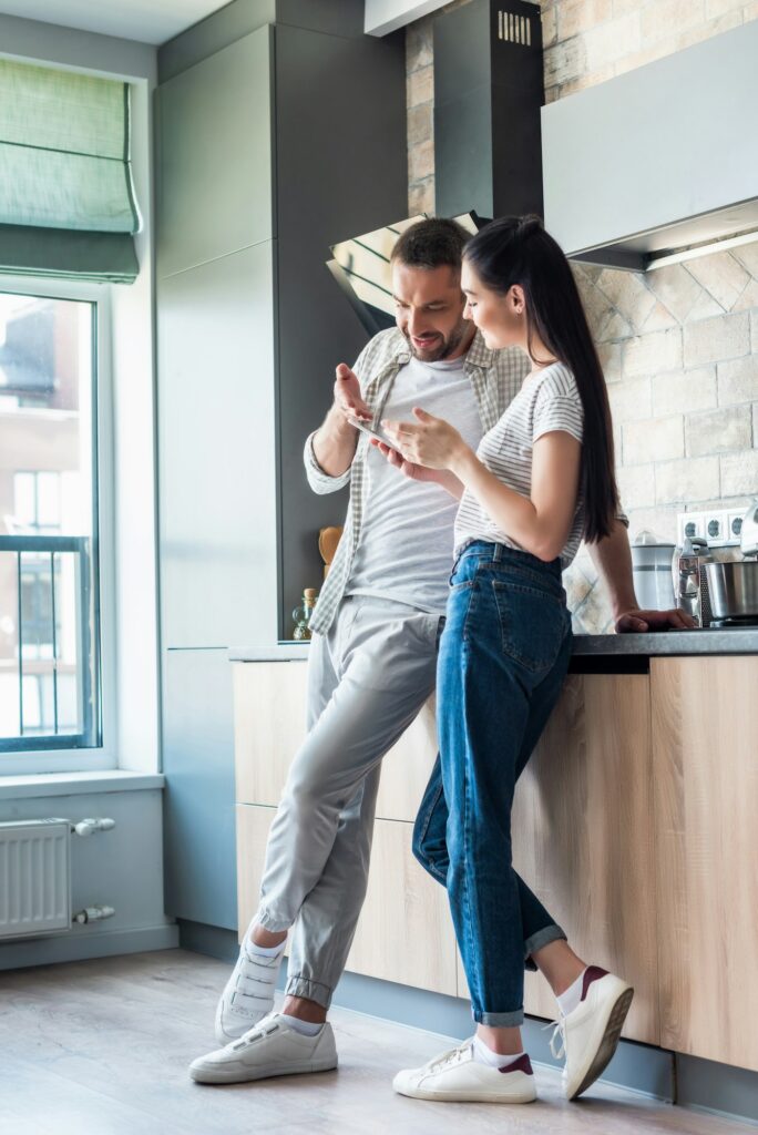 couple using smartphone together in kitchen, smart home concept